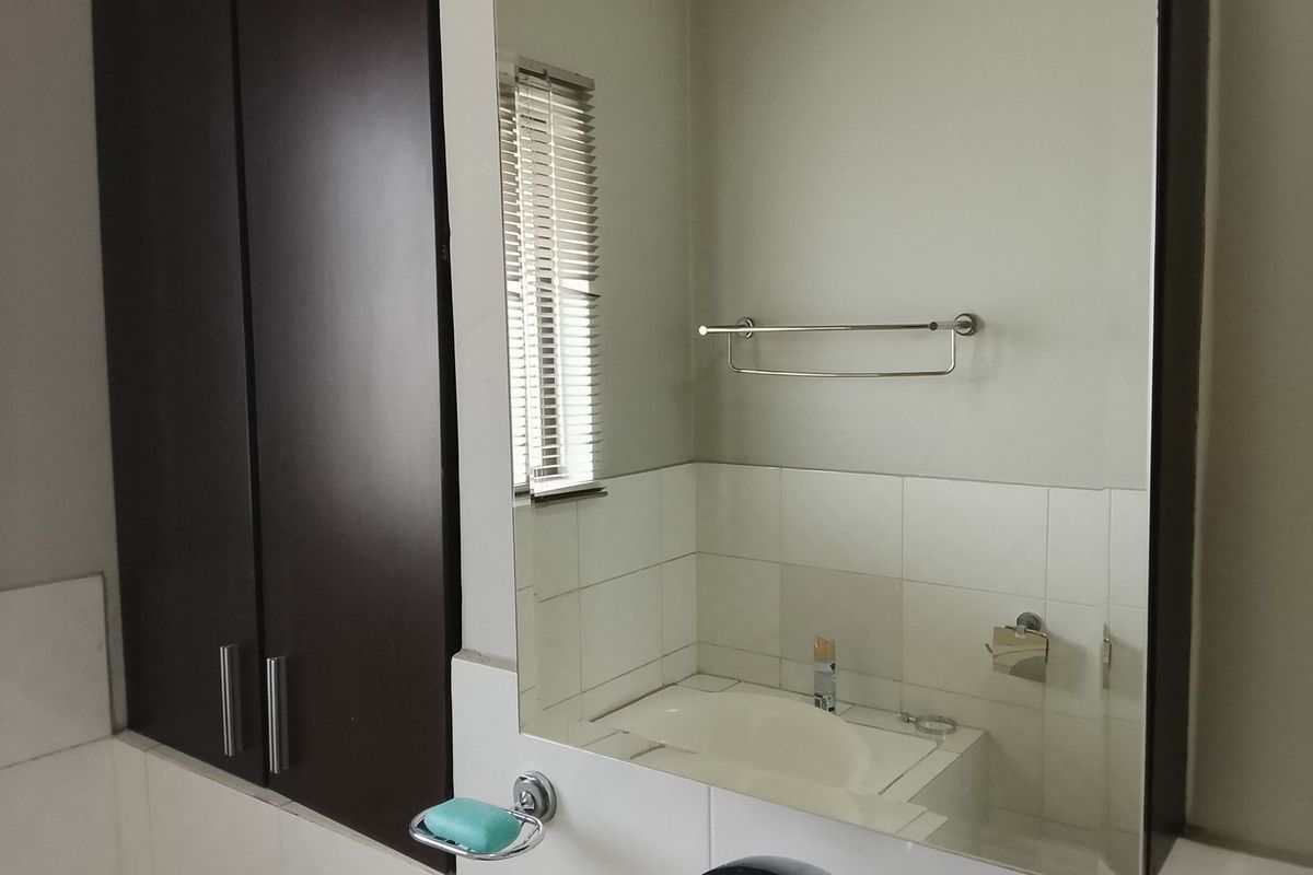 A clean bathroom featuring a built-in vanity cupboard, large wall-mounted mirror, and functional chrome fixtures including a towel rail and soap dish.