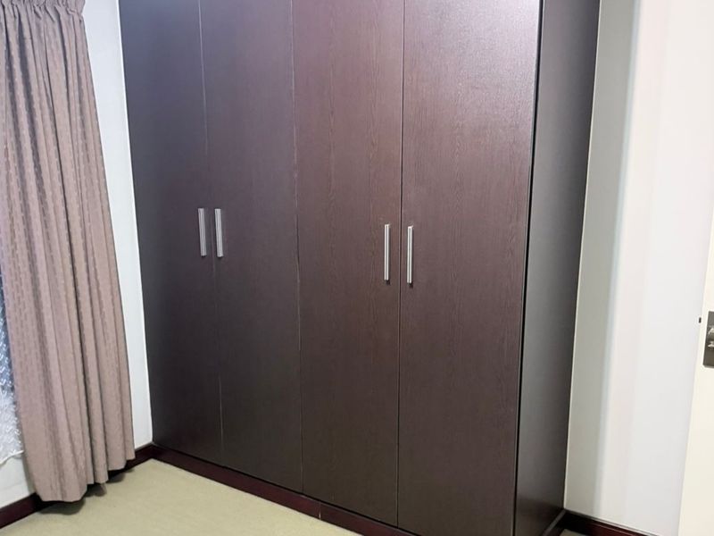 A bedroom featuring dark wood-finish built-in cupboards with modern metal handles.