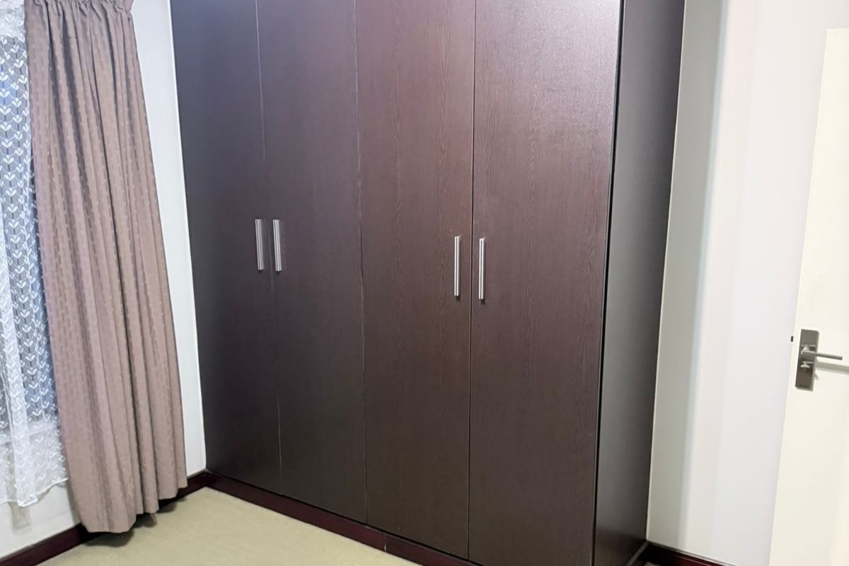 A bedroom featuring dark wood-finish built-in cupboards with modern metal handles.