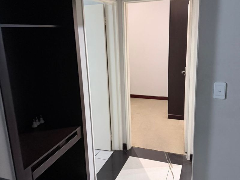 A functional hallway connecting interior spaces, featuring built-in storage cabinetry, a mix of tiled and carpeted flooring, and neutral wall finishes.