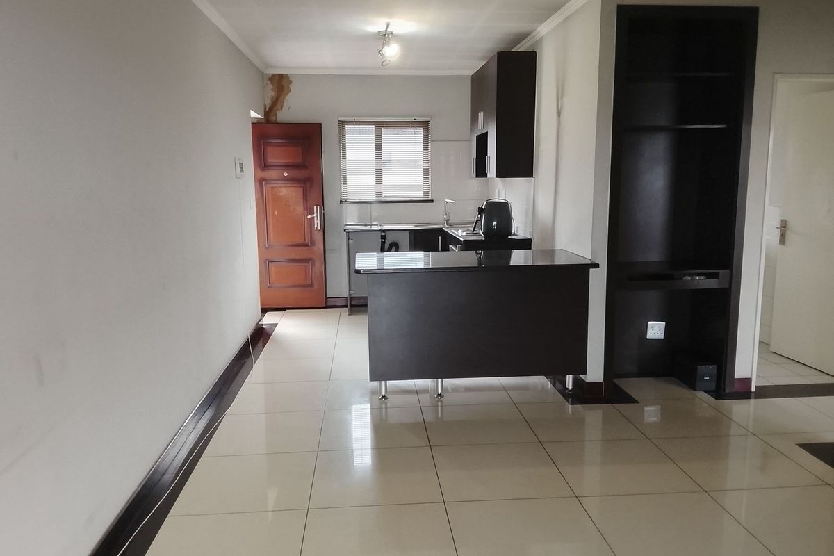 Open plan kitchen and living area featuring tiled floors, dark cabinetry, a breakfast bar, and built-in shelving, with visible wall damage near the entrance.