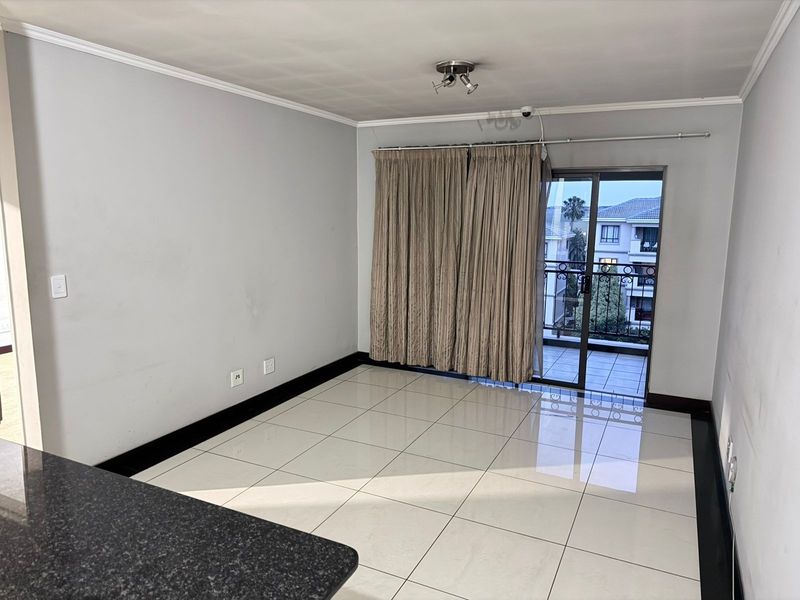 An open-plan living area featuring tiled floors, a granite breakfast counter, and sliding glass doors leading to a private balcony.
