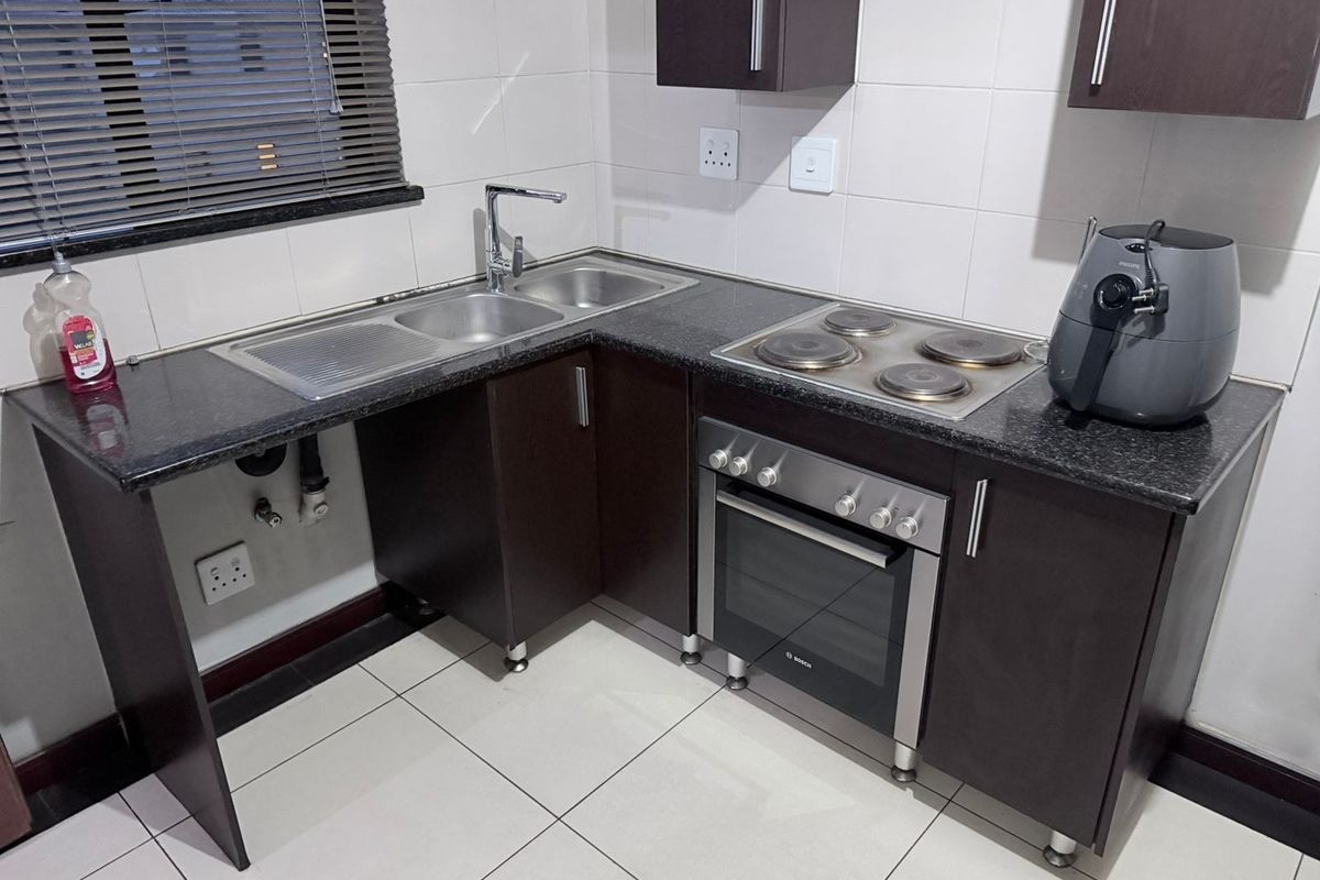 A compact, modern kitchen featuring dark cabinetry, granite countertops, a stainless steel sink, and a built-in electric oven and hob.