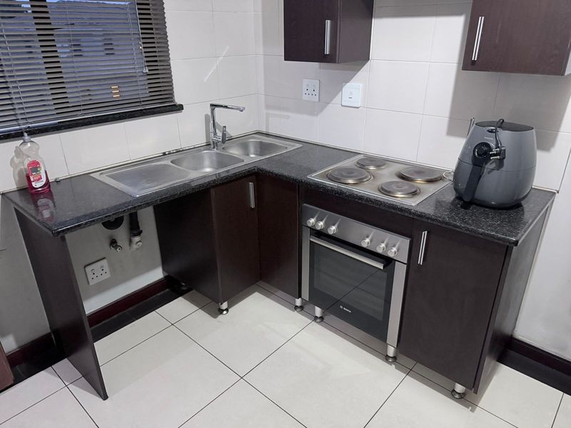 A compact, modern kitchen featuring dark cabinetry, granite countertops, a stainless steel sink, and a built-in electric oven and hob.