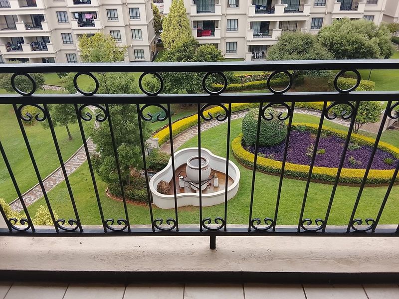 A balcony view overlooking a well-maintained communal garden with landscaped hedges, manicured lawns, and a central water feature.