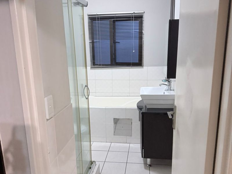 A functional bathroom featuring a shower enclosure, bathtub, vanity cabinet with basin, and tiled finishes throughout.