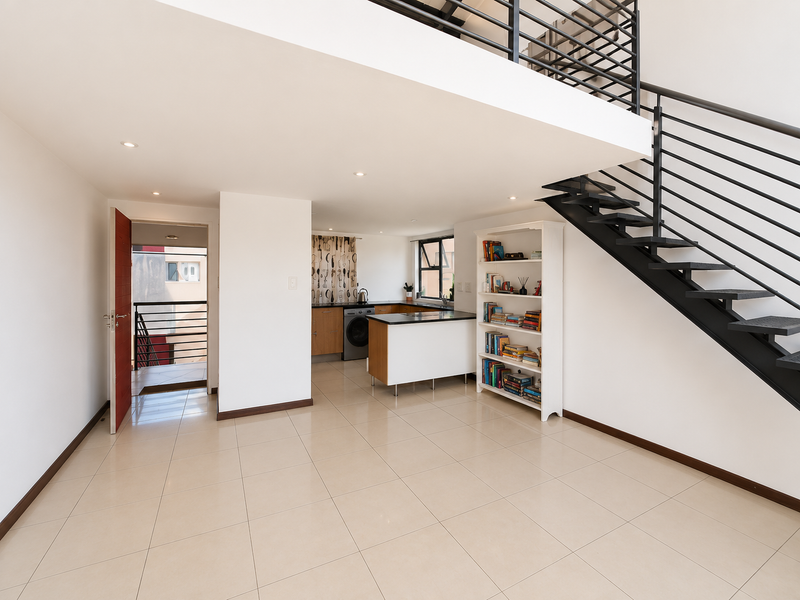 Open plan living area featuring tiled floors, a modern metal staircase with balustrade, and a compact kitchen with built-in cabinetry and island.