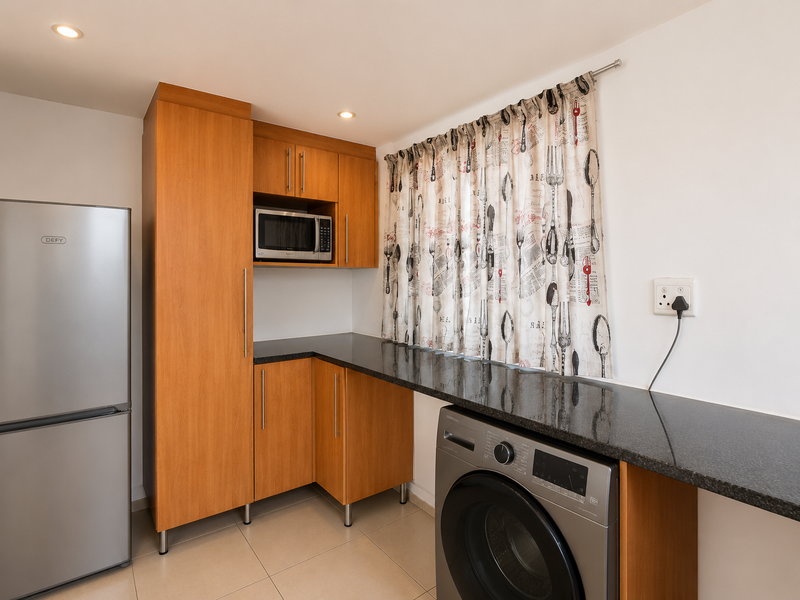 A functional laundry area featuring built-in wooden cabinetry, granite countertops, and space for a washing machine, complemented by recessed lighting and tiled floors.