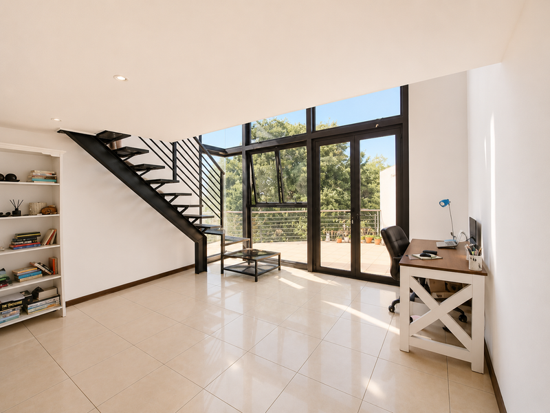 Bright living area featuring a modern metal staircase, large floor-to-ceiling windows, and direct access to a private balcony with tiled flooring.