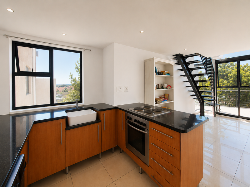 Modern open-plan kitchen featuring wooden cabinetry, black granite countertops, and a farmhouse sink, seamlessly connected to a staircase leading to the upper level.