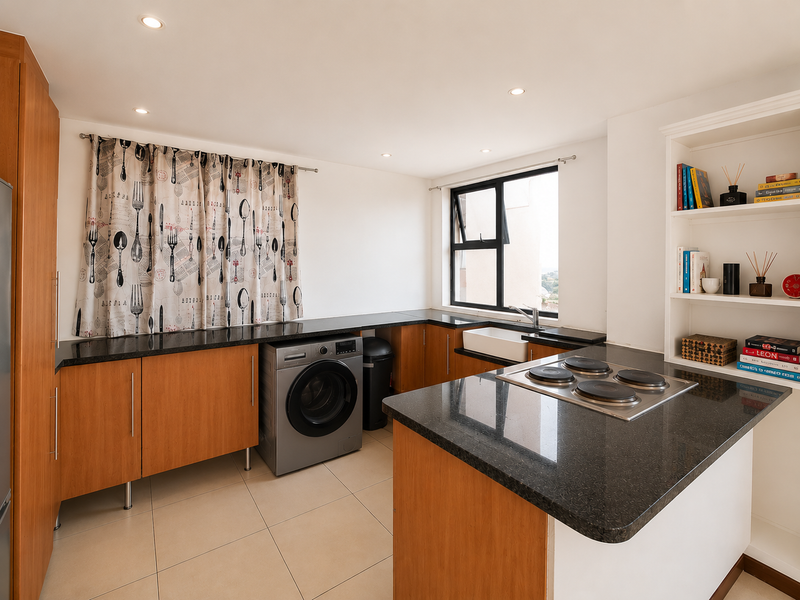 A functional kitchen featuring wood-finish cabinetry, dark granite countertops, an integrated electric hob, and a classic apron sink with ample storage space.