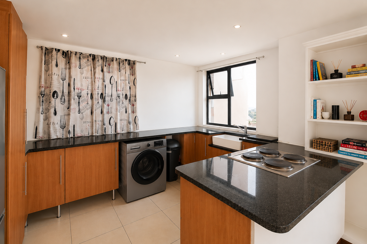 A functional kitchen featuring wood-finish cabinetry, dark granite countertops, an integrated electric hob, and a classic apron sink with ample storage space.