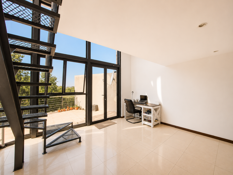 Bright living area featuring a modern metal spiral staircase, large floor-to-ceiling windows, and direct access to an outdoor balcony space.
