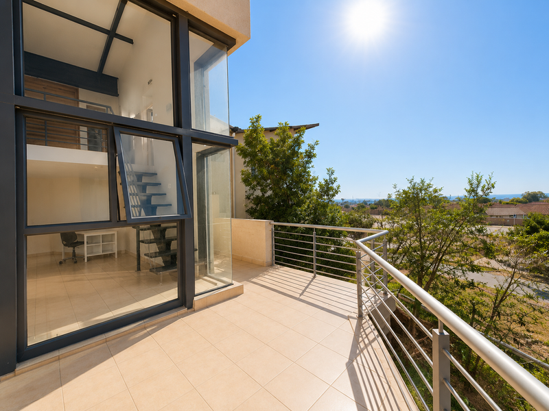 A spacious balcony with tiled flooring and a modern metal balustrade, offering views and direct access to a multi-level interior space.