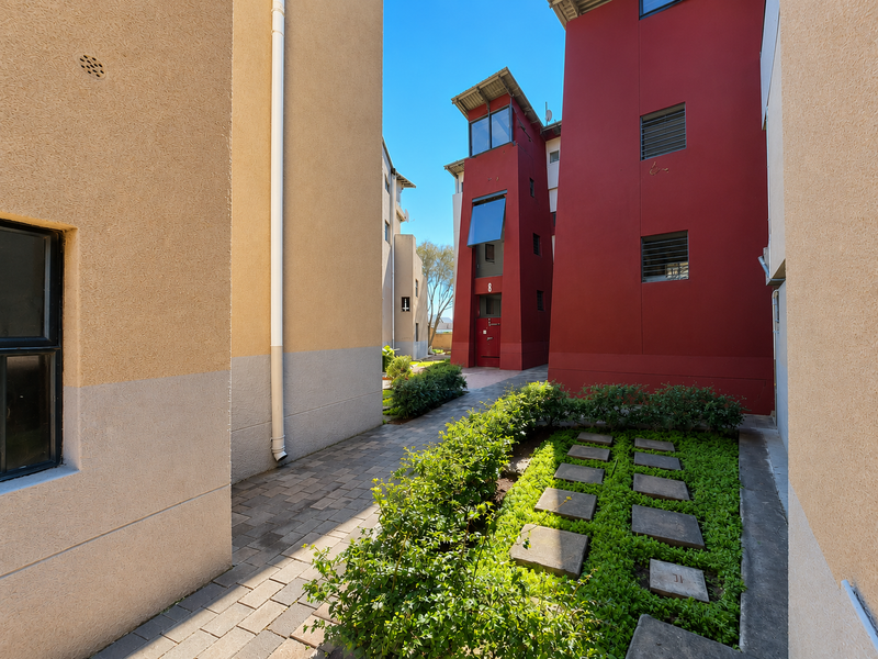 A view of the apartment complex exterior featuring paved walkways, landscaped garden beds with stone stepping stones, and modern multi-story building facades.