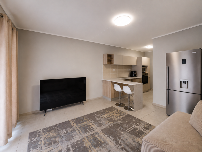 Modern open-plan living area featuring a sleek kitchen with breakfast bar, built-in appliances, and neutral tiled flooring throughout.