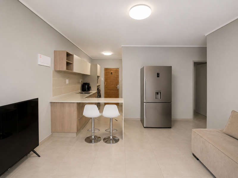 Modern open-plan living area featuring a sleek kitchen with built-in cabinetry, stone countertops, and neutral tiled flooring throughout.