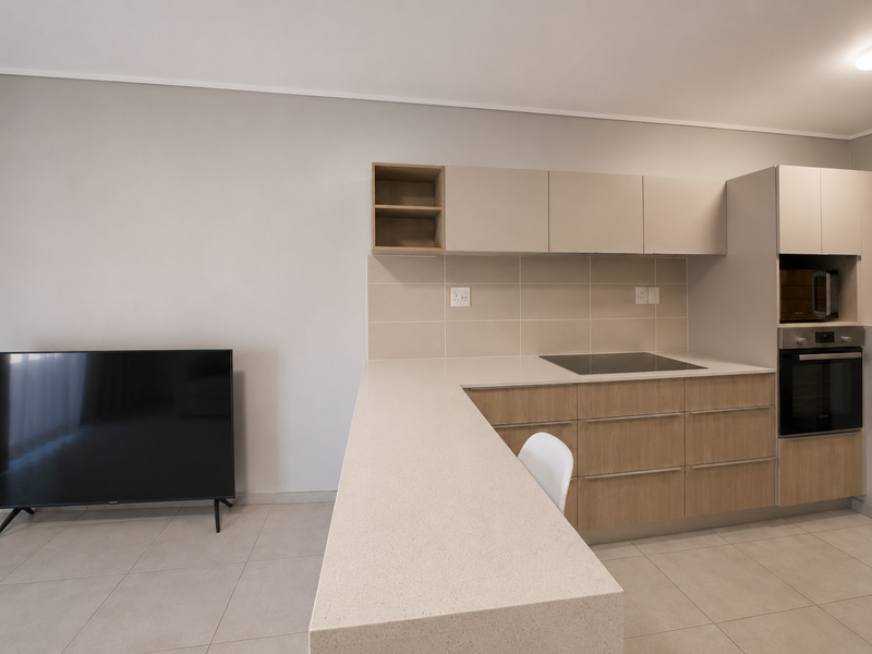 Modern open-plan kitchen featuring sleek cabinetry, stone countertops, a breakfast bar, and integrated appliances, seamlessly flowing into the living area.