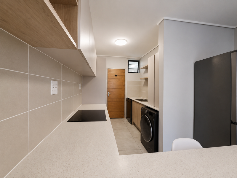 Modern kitchen featuring sleek cabinetry, stone countertops, an electric hob, and a tiled backsplash, offering a clean and functional workspace.