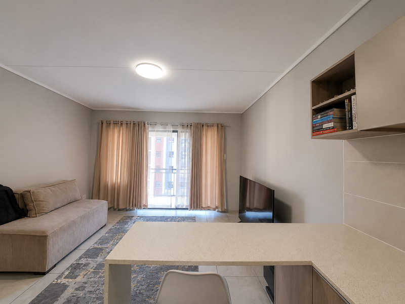 Open plan living area featuring tiled flooring, a built-in stone countertop workspace, and a sliding glass door leading to a balcony.
