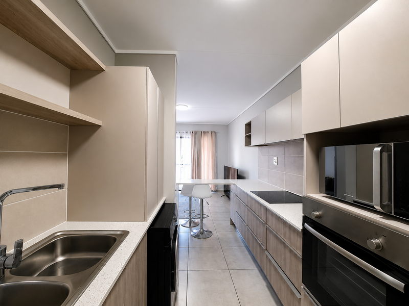 Modern open-plan kitchen featuring sleek cabinetry, stone countertops, integrated appliances, and tiled flooring, flowing seamlessly into the adjacent living area.