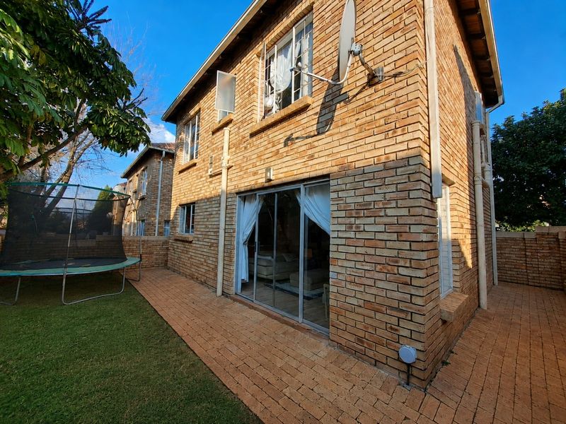 Rear view of a face brick townhouse featuring a paved patio area, small lawn, and sliding glass door access to the interior living space.