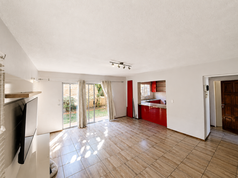 Open-plan living area featuring tiled flooring, sliding doors to the garden, and a connected kitchen with red cabinetry and a breakfast bar.