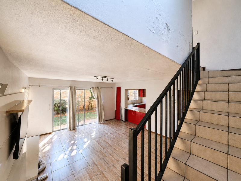 Open-plan living area featuring tiled floors, a staircase with metal railing, and sliding doors leading to the garden, with a connected kitchen space.