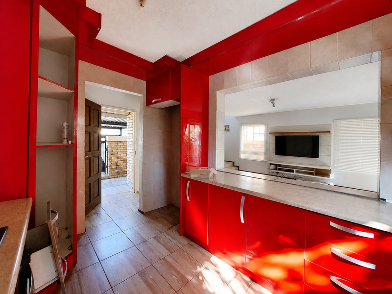 A kitchen area featuring red cabinetry, tiled flooring, and a pass-through window looking into the living space.