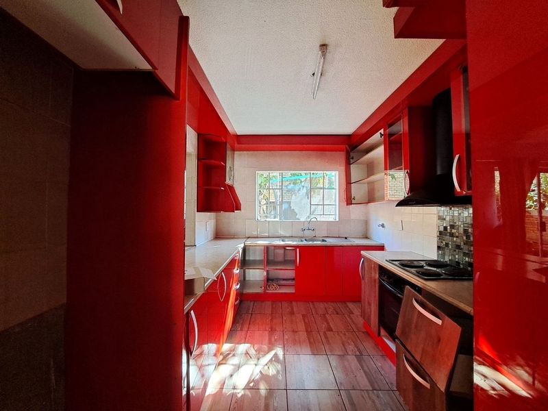A dated kitchen featuring red cabinetry, built-in oven and hob, tiled backsplash, and tiled flooring, currently vacant and in need of cosmetic updates.