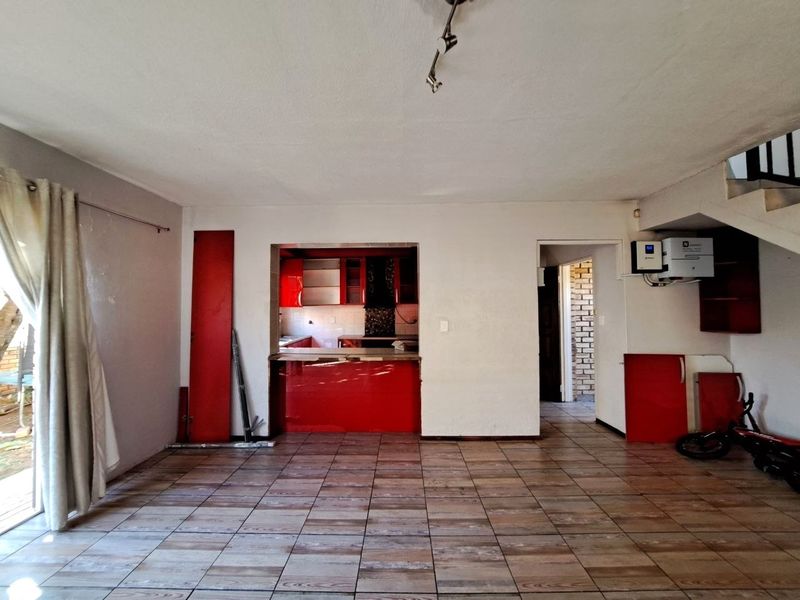 Open plan living area featuring tiled floors, a kitchen with red cabinetry, and an integrated inverter system, offering a blank canvas for renovation.