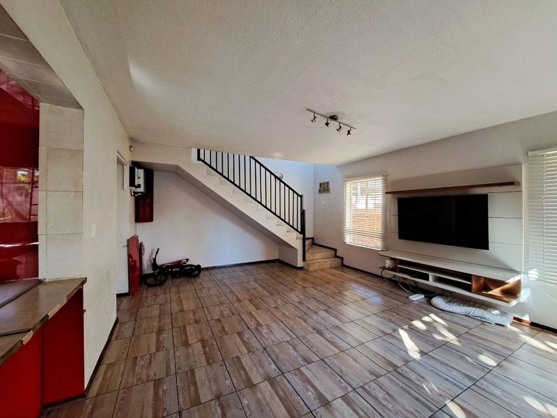 Open plan living area featuring wood-look tiled flooring, a staircase with metal balustrades, and a built-in media unit.