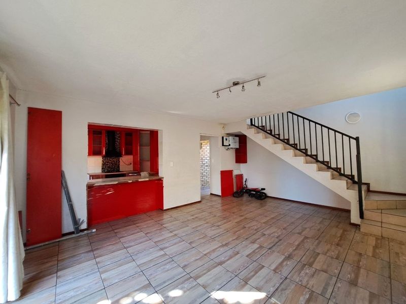 Open plan living area featuring tiled floors, a staircase with metal balustrade, and a dated kitchen with red cabinetry.