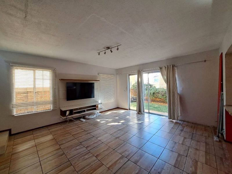 Spacious living room featuring tiled flooring, built-in media console, and sliding glass doors providing direct access to the rear garden area.