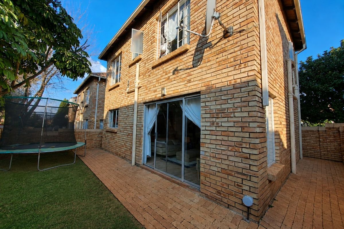 Rear view of a face brick townhouse featuring a paved patio area, small lawn, and sliding glass door access to the interior living space.