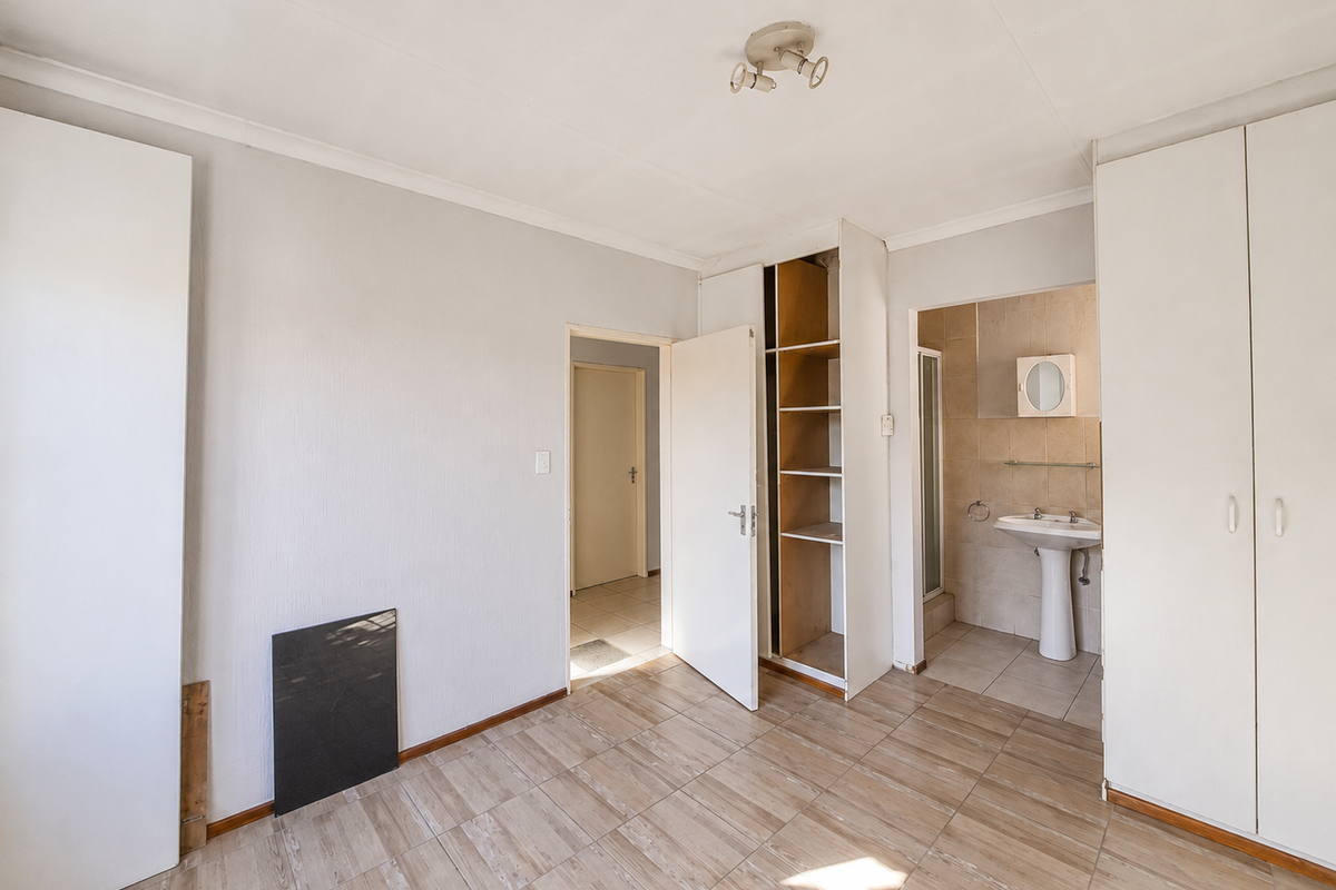 An empty bedroom featuring built-in cupboards, tiled flooring, and an en-suite bathroom with a pedestal basin and shower.