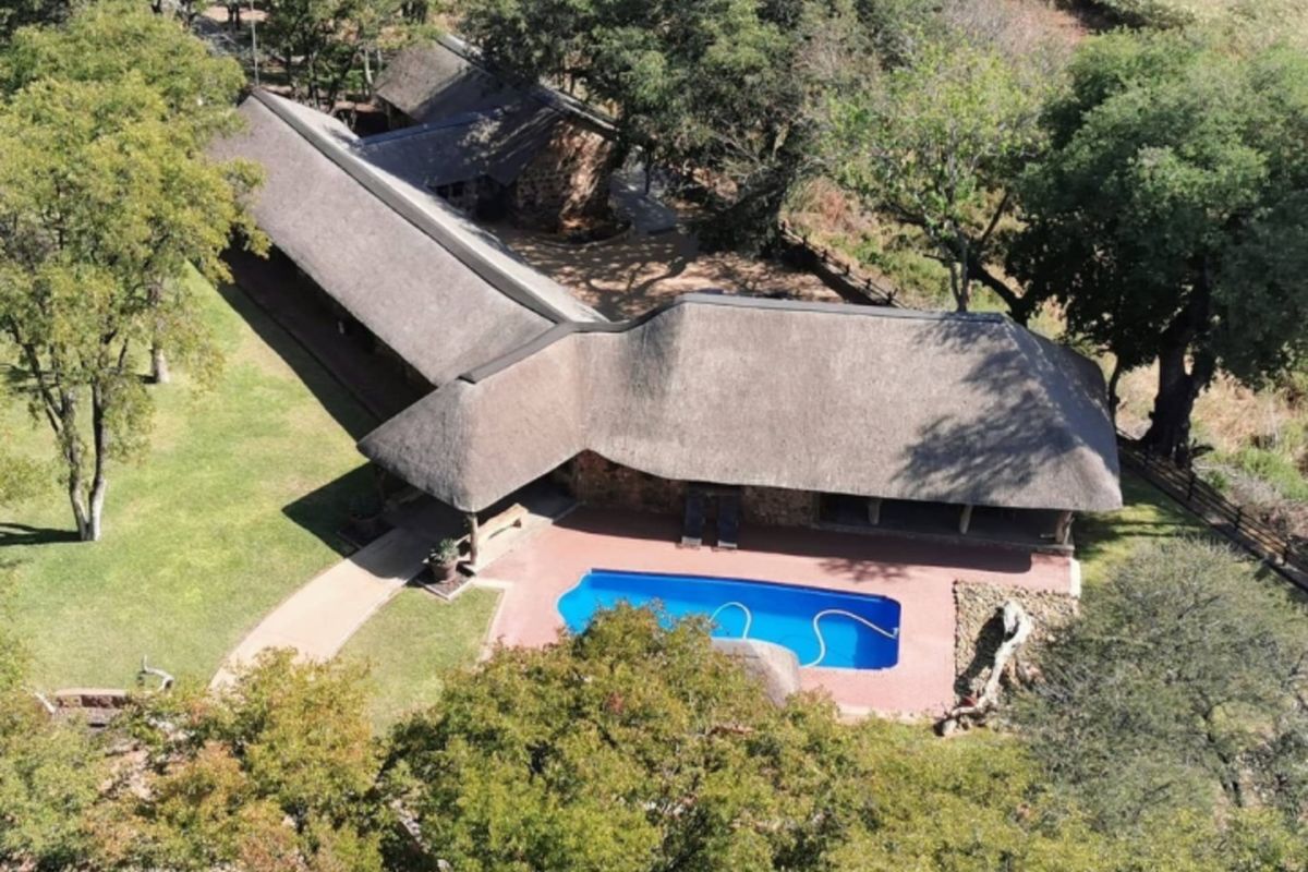 Aerial view of a farm property featuring a large thatched-roof residence, a swimming pool, and surrounding mature trees and landscaped grounds.