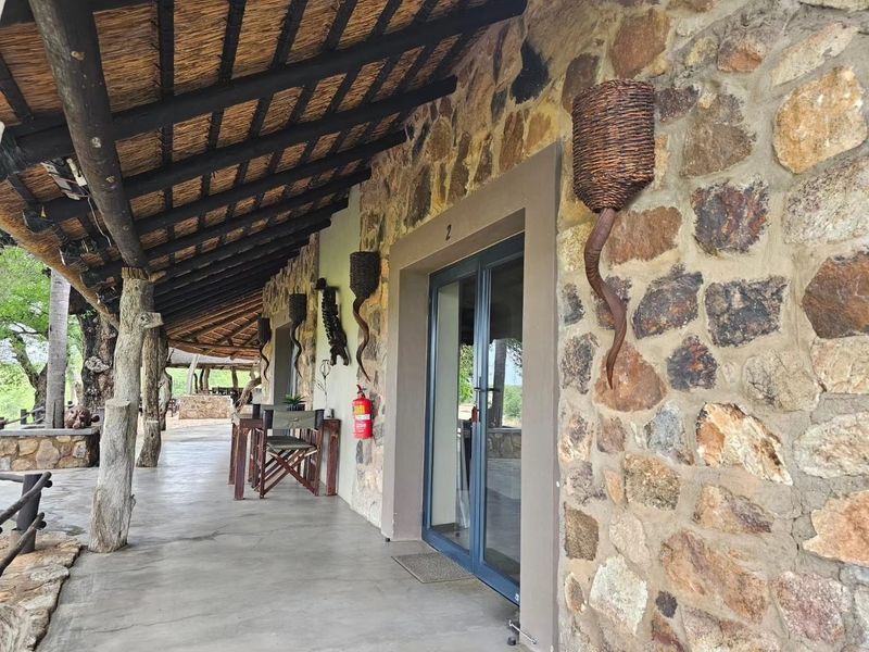 A covered patio area featuring rustic stone walls, a traditional thatched roof, and glass sliding door access to the interior.