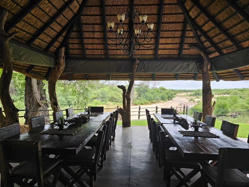 An expansive covered outdoor entertainment area featuring a traditional thatched roof, rustic timber supports, and scenic views over the surrounding landscape.