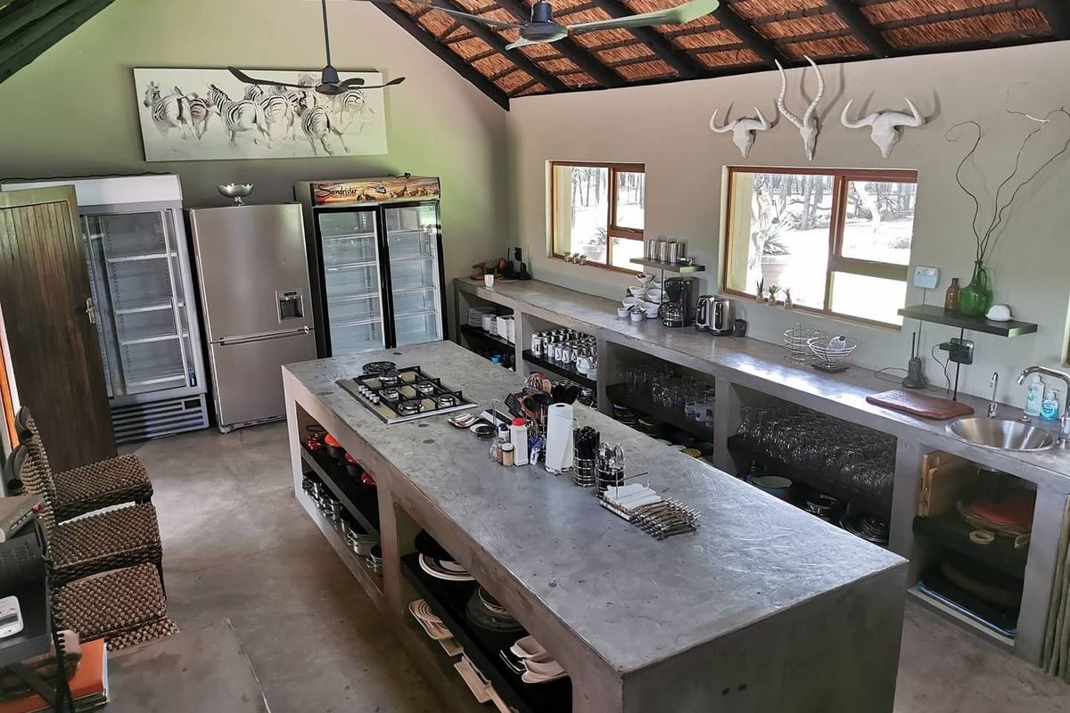 Spacious rustic kitchen featuring a large concrete island with integrated gas hob, concrete countertops, and exposed thatch ceiling with ceiling fans.