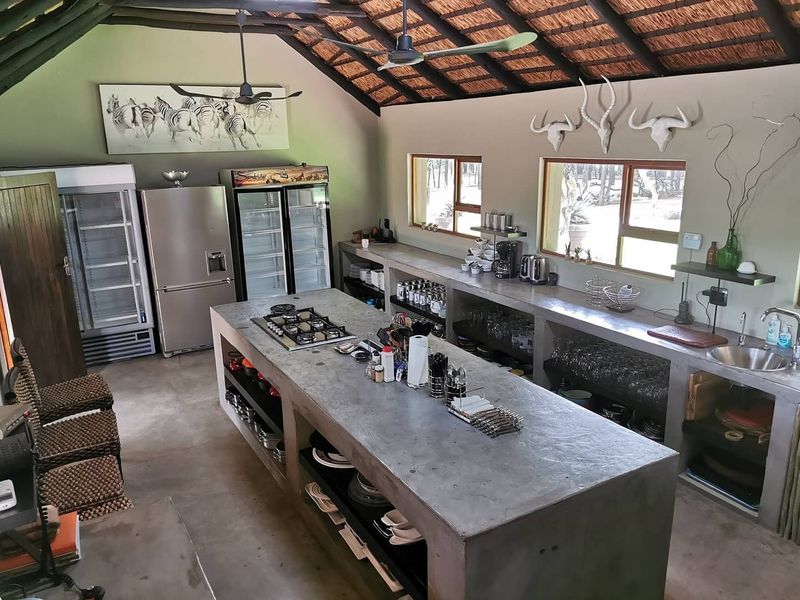 Spacious rustic kitchen featuring a large concrete island with integrated gas hob, concrete countertops, and exposed thatch ceiling with ceiling fans.