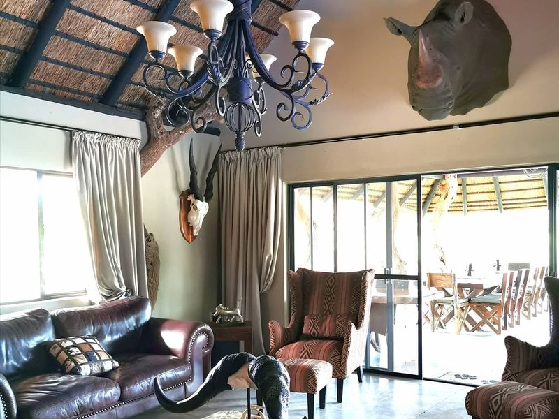 Spacious living area featuring a high thatched ceiling with exposed timber beams, polished concrete floors, and large sliding doors opening to an outdoor patio.