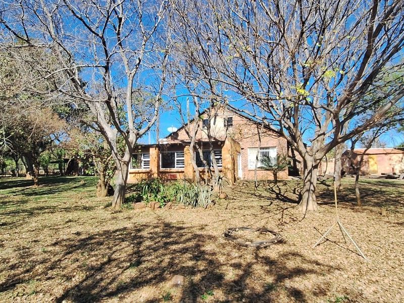 Rear view of a brick farmhouse set within a large, mature garden with established trees and natural landscaping.