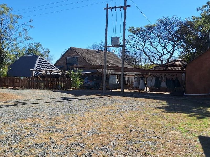 A wide view of the farm property entrance featuring a gravel driveway, utility infrastructure, and multiple outbuildings with tiled roofing.