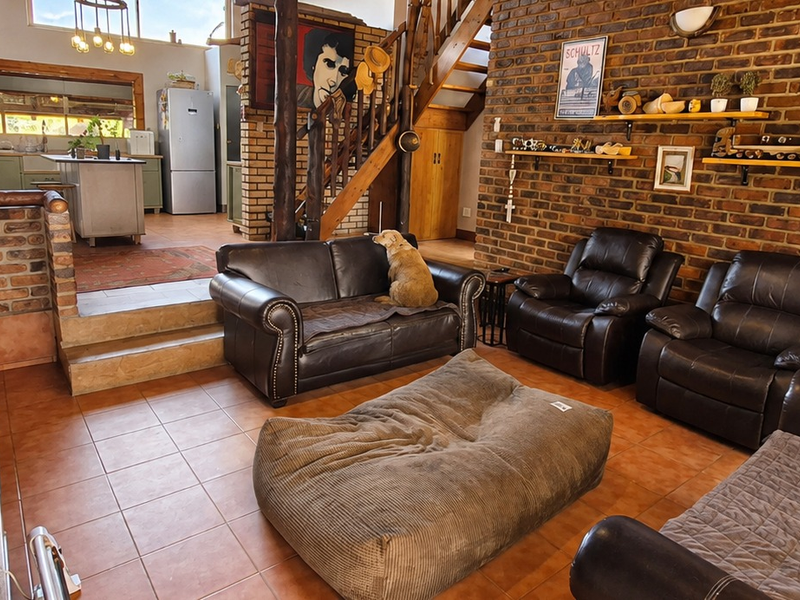 Spacious open-plan living area featuring exposed brick walls, a wooden staircase, and an adjoining kitchen with island cabinetry and tiled flooring.