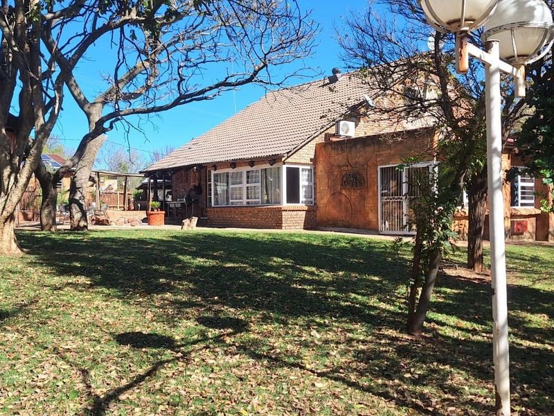 Rear view of a brick farmhouse featuring a tiled roof, established garden with mature trees, and an exterior air conditioning unit.
