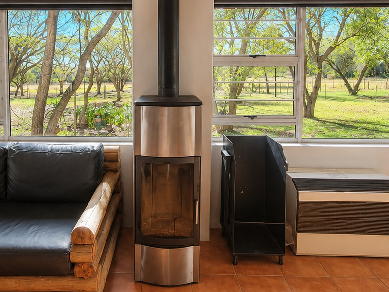 A bright living area featuring a modern freestanding fireplace, tiled flooring, and large windows offering scenic views of the surrounding farm landscape.