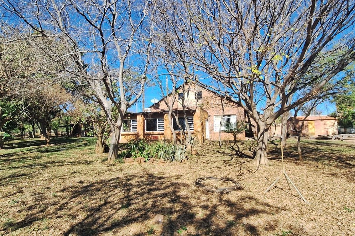 Rear view of a brick farmhouse set within a large, mature garden with established trees and natural landscaping.