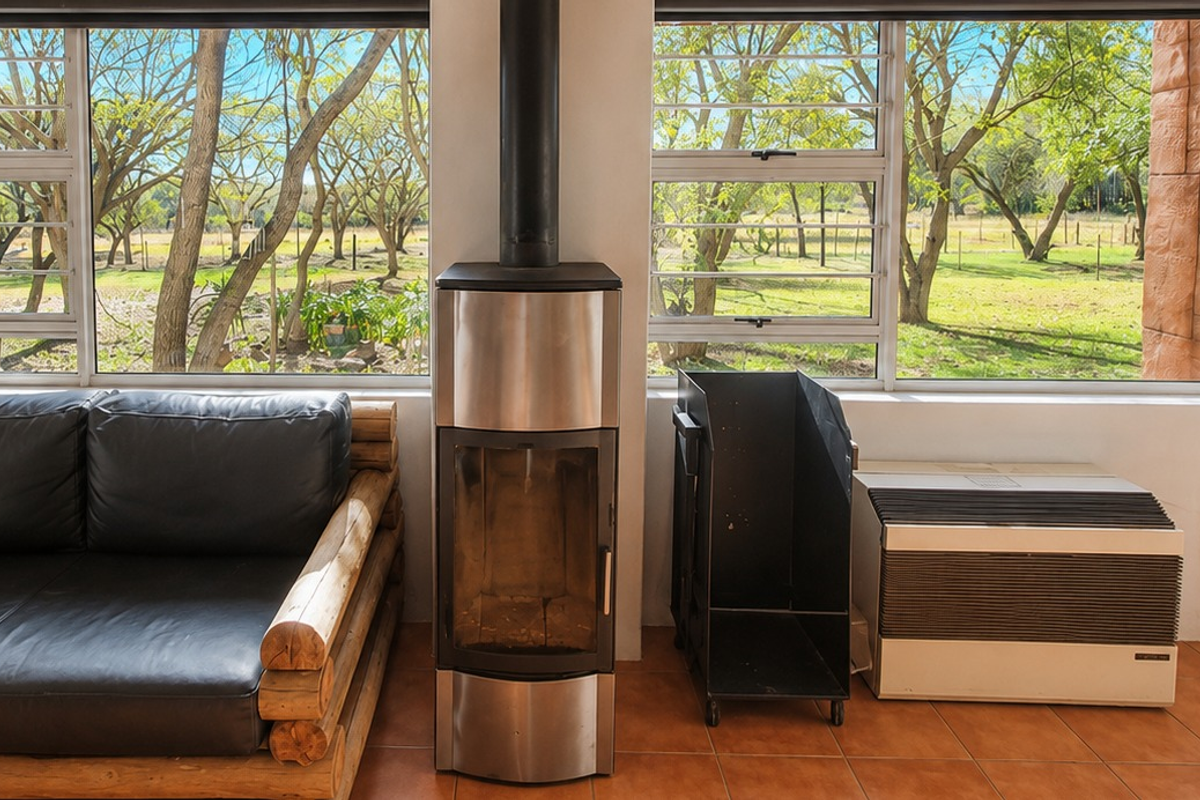 A bright living area featuring a modern freestanding fireplace, tiled flooring, and large windows offering scenic views of the surrounding farm landscape.