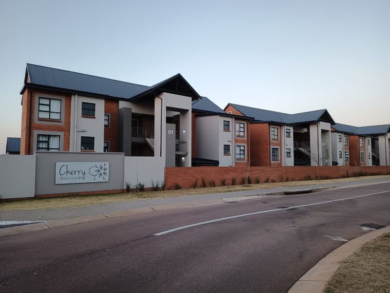 Street view of the Cherry Blossom townhouse complex featuring modern brick and plaster architecture with metal roofing and secure boundary walls.